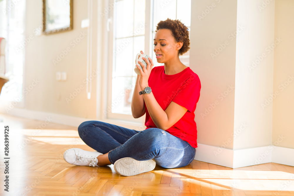 Beautiful young african american woman sitting on the floor at home and drinking a cup of coffee Beautiful young african american woman sitting on the floor at home and drinking a cup of coffee