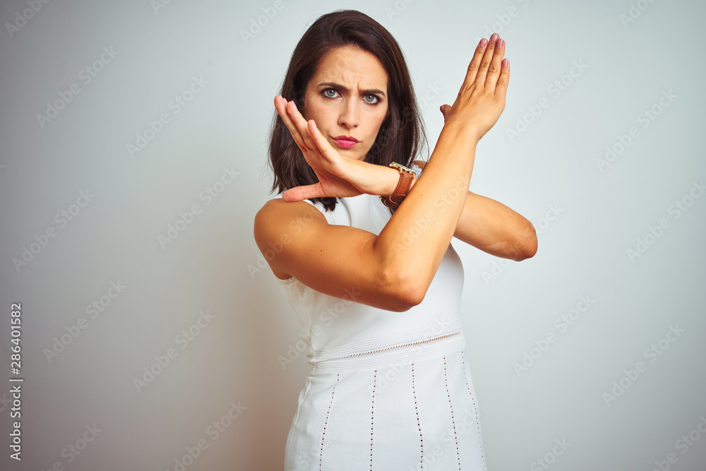 Obraz premium Young beautiful woman wearing dress standing over white isolated background Rejection expression crossing arms doing negative sign, angry face