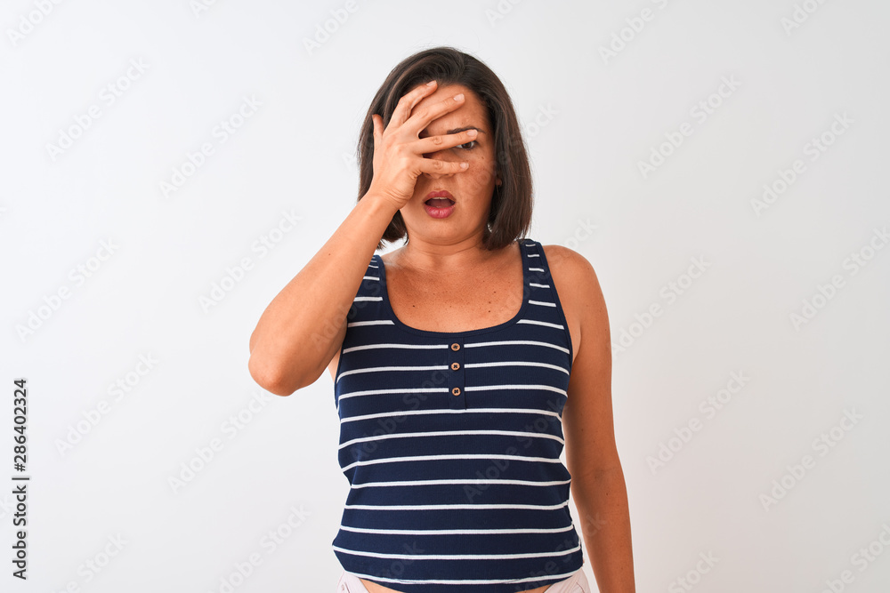 Young beautiful woman wearing blue striped t-shirt standing over isolated white background peeking in shock covering face and eyes with hand, looking through fingers with embarrassed expression. Young beautiful woman wearing blue striped t-shirt standing over isolated white background peeking in shock covering face and eyes with hand, looking through fingers with embarrassed expression.
