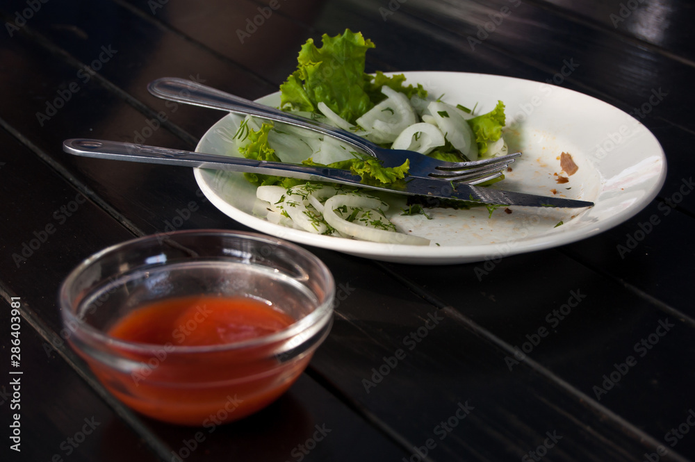 leftover lettuce and onion rings on white plate with fork and knife next to red sauce bar leftover lettuce and onion rings on white plate with fork and knife next to red sauce bar