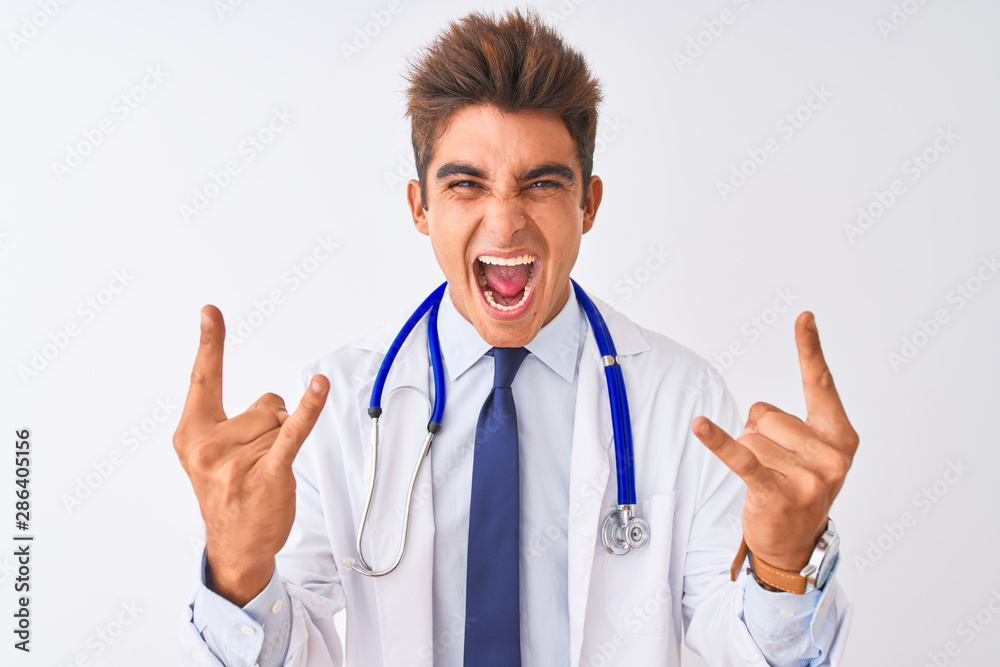 Young handsome doctor man wearing stethoscope over isolated white background shouting with crazy expression doing rock symbol with hands up. Music star. Heavy concept. Young handsome doctor man wearing stethoscope over isolated white background shouting with crazy expression doing rock symbol with hands up. Music star. Heavy concept.