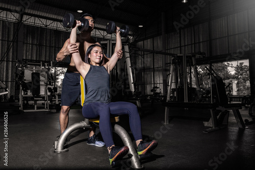 Young sport man and woman with dumbbells flexing muscles in gym. photo