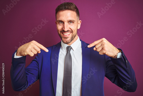 Young handsome business man over purple isolated background looking confident with smile on face, pointing oneself with fingers proud and happy.