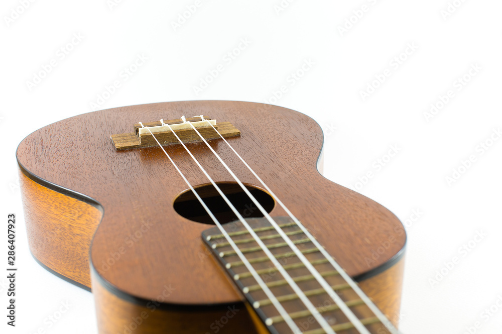 Close-up head of dark wooden ukulele music instrument Hawaiian guitar body with selected focus and copy space isolated over white background. Close-up head of dark wooden ukulele music instrument Hawaiian guitar body with selected focus and copy space isolated over white background.