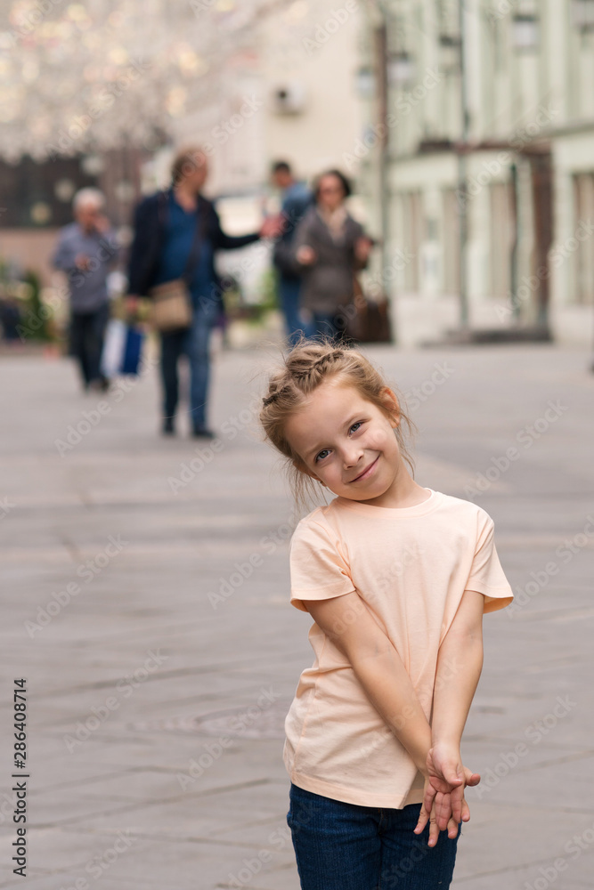 Cute little naughty girl walking through the city streets and posing for the camera. Time of prank. Urban casual outfit. Carefree. Happiness, fun and childhood concept.
