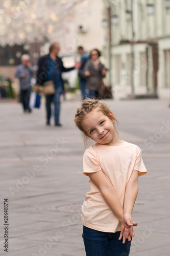 Cute little naughty girl walking through the city streets and posing for the camera. Time of prank. Urban casual outfit. Carefree. Happiness, fun and childhood concept. photo