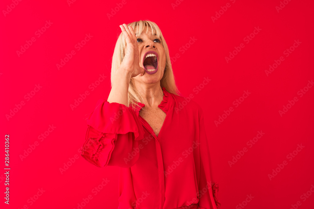 Middle age woman wearing elegant shirt standing over isolated red background shouting and screaming loud to side with hand on mouth. Communication concept. Middle age woman wearing elegant shirt standing over isolated red background shouting and screaming loud to side with hand on mouth. Communication concept.