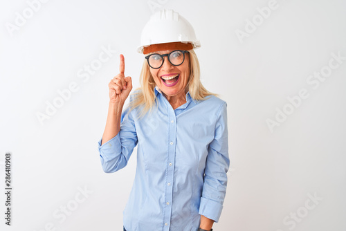 Middle age architect woman wearing glasses and helmet over isolated white background pointing finger up with successful idea. Exited and happy. Number one.