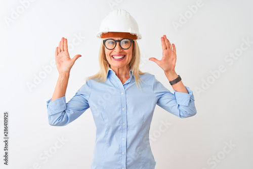 Middle age architect woman wearing glasses and helmet over isolated white background showing and pointing up with fingers number ten while smiling confident and happy.