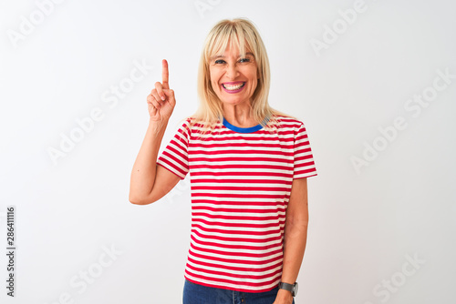 Middle age woman wearing casual striped t-shirt standing over isolated white background showing and pointing up with finger number one while smiling confident and happy.