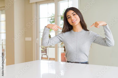 Young beautiful woman at home looking confident with smile on face  pointing oneself with fingers proud and happy.