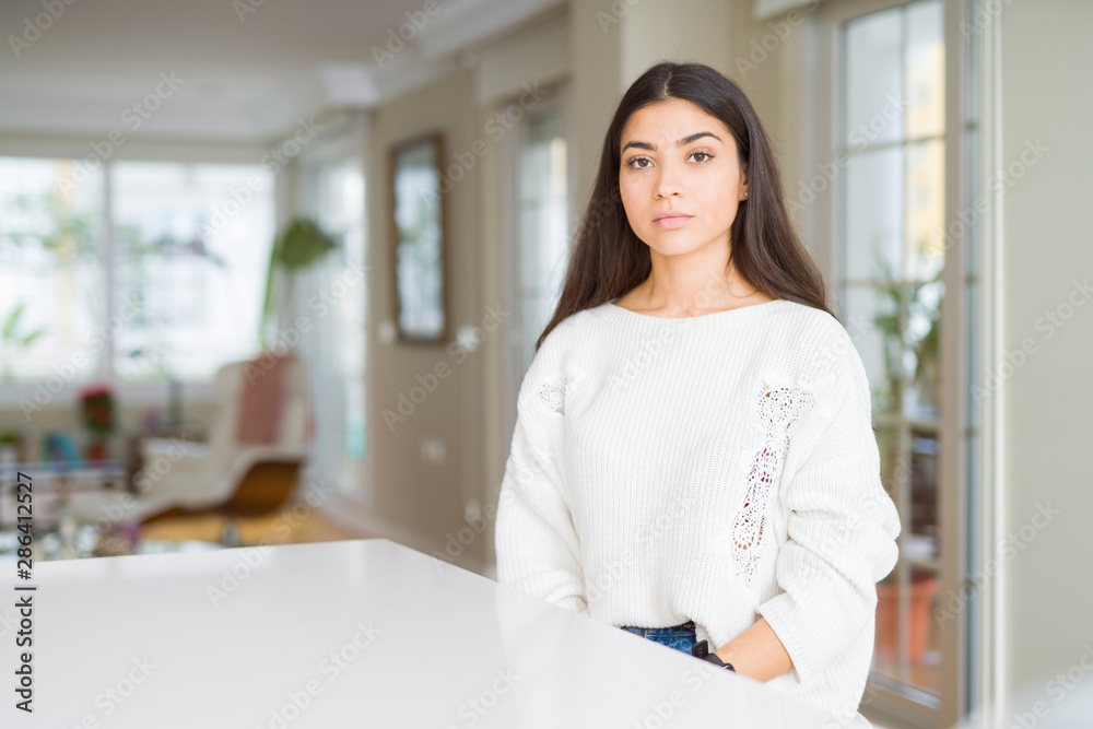Young beautiful woman at home on white table with serious expression on face. Simple and natural looking at the camera. Young beautiful woman at home on white table with serious expression on face. Simple and natural looking at the camera.