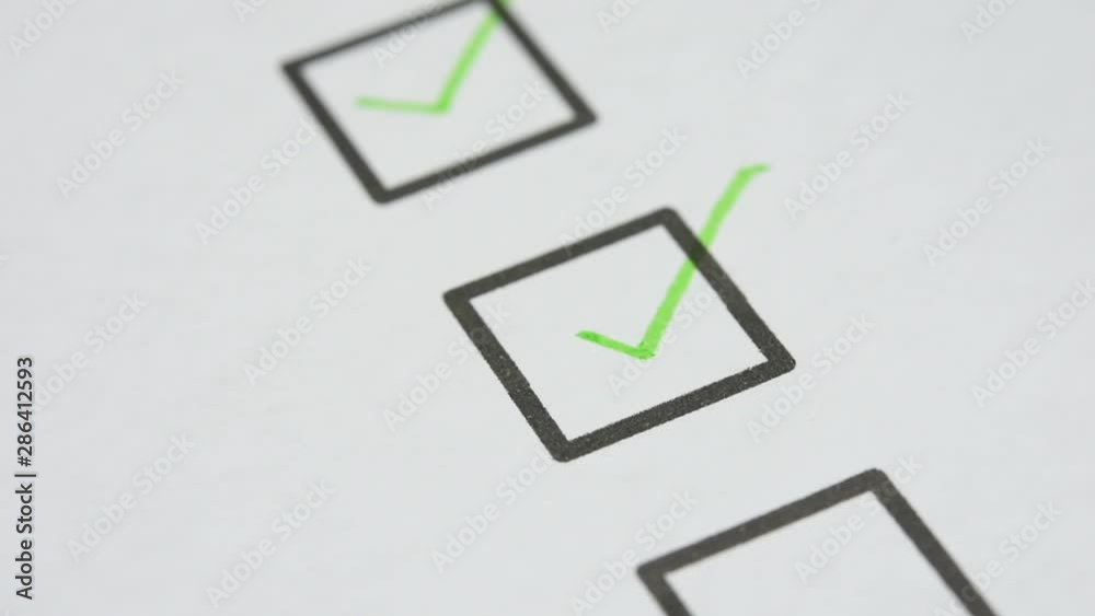green ink pen make a check mark sign in check box list on white paper. closed up and selective focus
