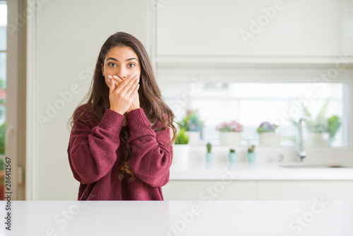 Young beautiful woman at home shocked covering mouth with hands for mistake. Secret concept.