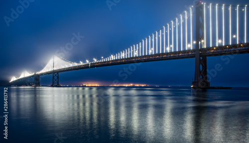 San Francisco Bay Bridge at night with deep blue sky and hazy lights in the fog