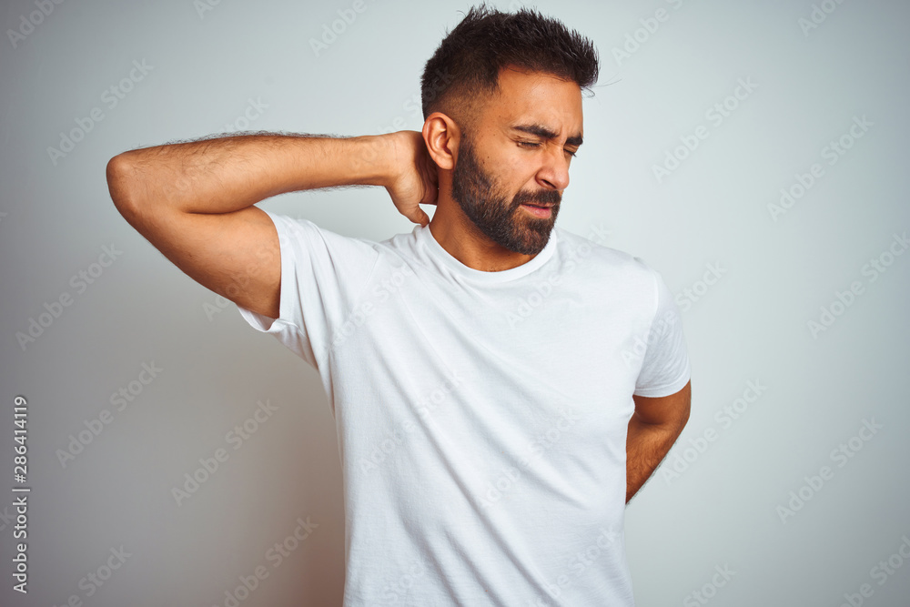 Young indian man wearing t-shirt standing over isolated white background Suffering of neck ache injury, touching neck with hand, muscular pain Young indian man wearing t-shirt standing over isolated white background Suffering of neck ache injury, touching neck with hand, muscular pain