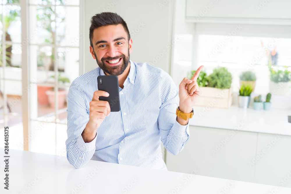 Handsome hispanic business man using smartphone very happy pointing with hand and finger to the side