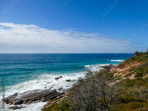 Bright sunny summer beach day with vivid blue ocean in the background and cliffs in the foreground at Point Arkwright, Sunshine Coast, Queensland, Australia