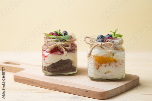 Raspberry cake in glass jar with fresh fruit and cream cheese on wooden background.