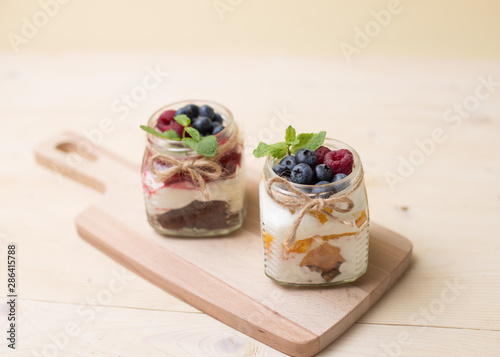 Raspberry cake in glass jar with fresh fruit and cream cheese on wooden background.