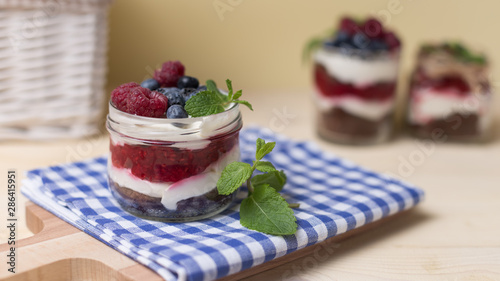 Raspberry cakes in glass jar with fresh fruit and cream cheese on a blue napkin.