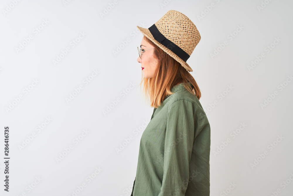 Redhead woman wearing green shirt glasses and hat over isolated white background looking to side, relax profile pose with natural face with confident smile. Redhead woman wearing green shirt glasses and hat over isolated white background looking to side, relax profile pose with natural face with confident smile.
