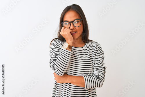 Young chinese woman wearing striped t-shirt and glasses over isolated white background looking stressed and nervous with hands on mouth biting nails. Anxiety problem.