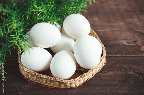 White chicken eggs in a wicker bowl on a dark wooden background