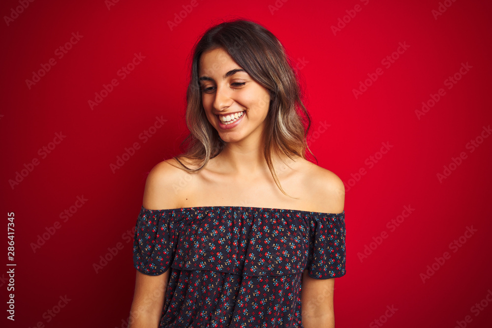 Young beautiful woman wearing a floral t-shirt over red isolated background looking away to side with smile on face, natural expression. Laughing confident. Young beautiful woman wearing a floral t-shirt over red isolated background looking away to side with smile on face, natural expression. Laughing confident.