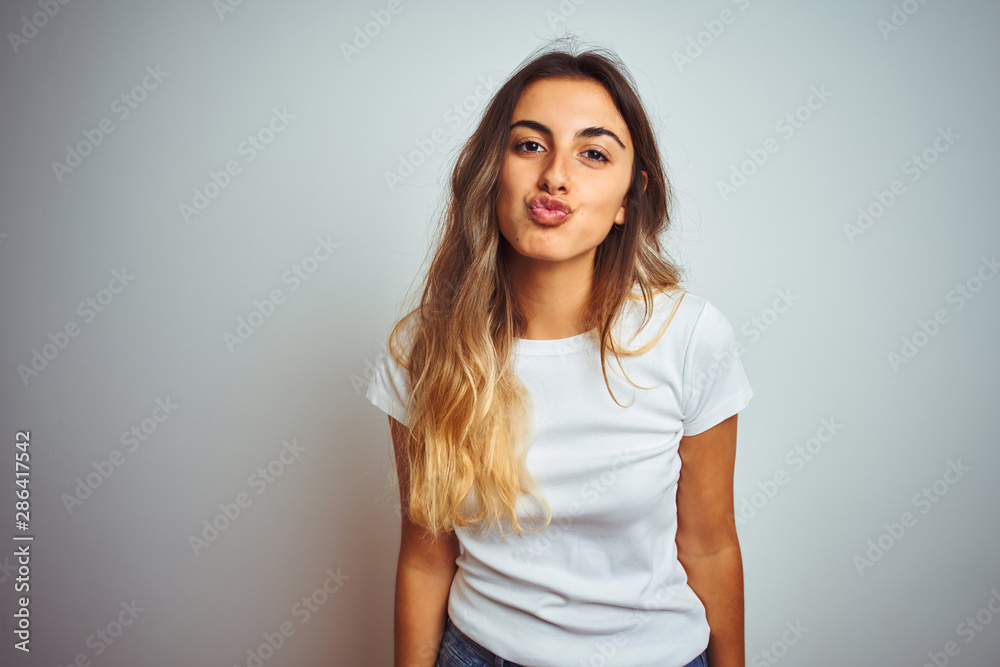 Young beautiful woman wearing casual white t-shirt over isolated background looking at the camera blowing a kiss on air being lovely and sexy. Love expression. Young beautiful woman wearing casual white t-shirt over isolated background looking at the camera blowing a kiss on air being lovely and sexy. Love expression.