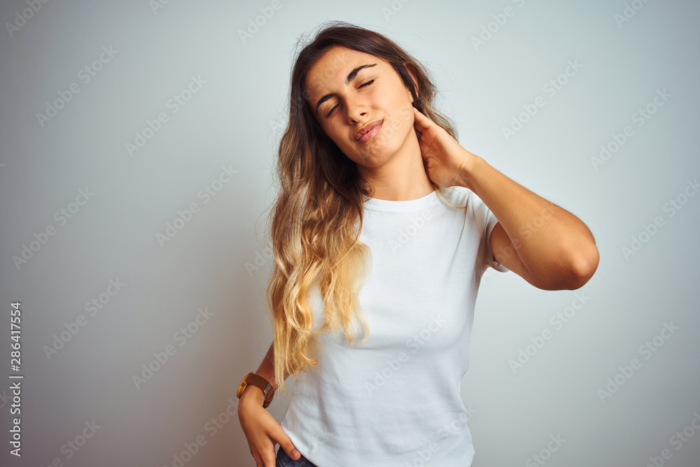 Young beautiful woman wearing casual white t-shirt over isolated background Suffering of neck ache injury, touching neck with hand, muscular pain Young beautiful woman wearing casual white t-shirt over isolated background Suffering of neck ache injury, touching neck with hand, muscular pain