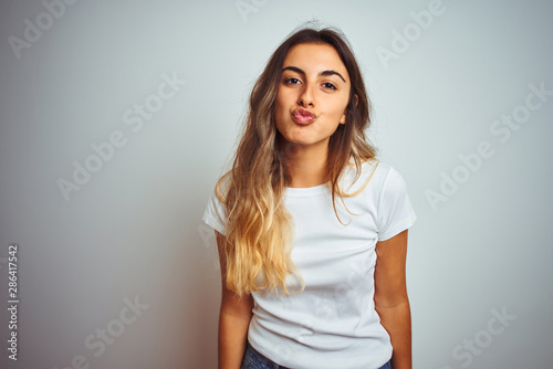 Young beautiful woman wearing casual white t-shirt over isolated background looking at the camera blowing a kiss on air being lovely and sexy. Love expression.