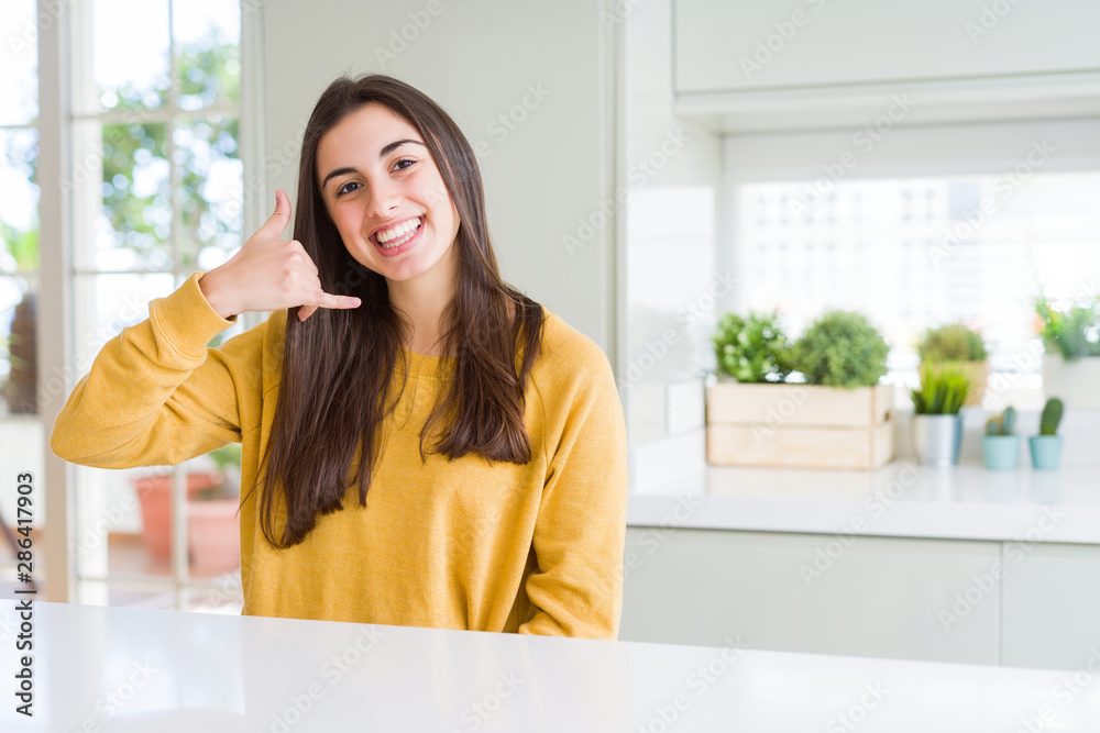 Beautiful young woman wearing yellow sweater smiling doing phone gesture with hand and fingers like talking on the telephone. Communicating concepts. Beautiful young woman wearing yellow sweater smiling doing phone gesture with hand and fingers like talking on the telephone. Communicating concepts.