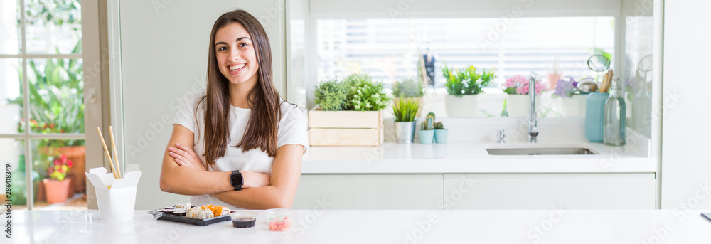 Wide angle picture of beautiful young woman eating asian sushi from delivery happy face smiling with crossed arms looking at the camera. Positive person. Wide angle picture of beautiful young woman eating asian sushi from delivery happy face smiling with crossed arms looking at the camera. Positive person.