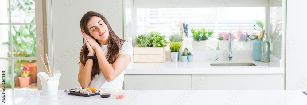 Wide angle picture of beautiful young woman eating asian sushi from delivery sleeping tired dreaming and posing with hands together while smiling with closed eyes. Wide angle picture of beautiful young woman eating asian sushi from delivery sleeping tired dreaming and posing with hands together while smiling with closed eyes.