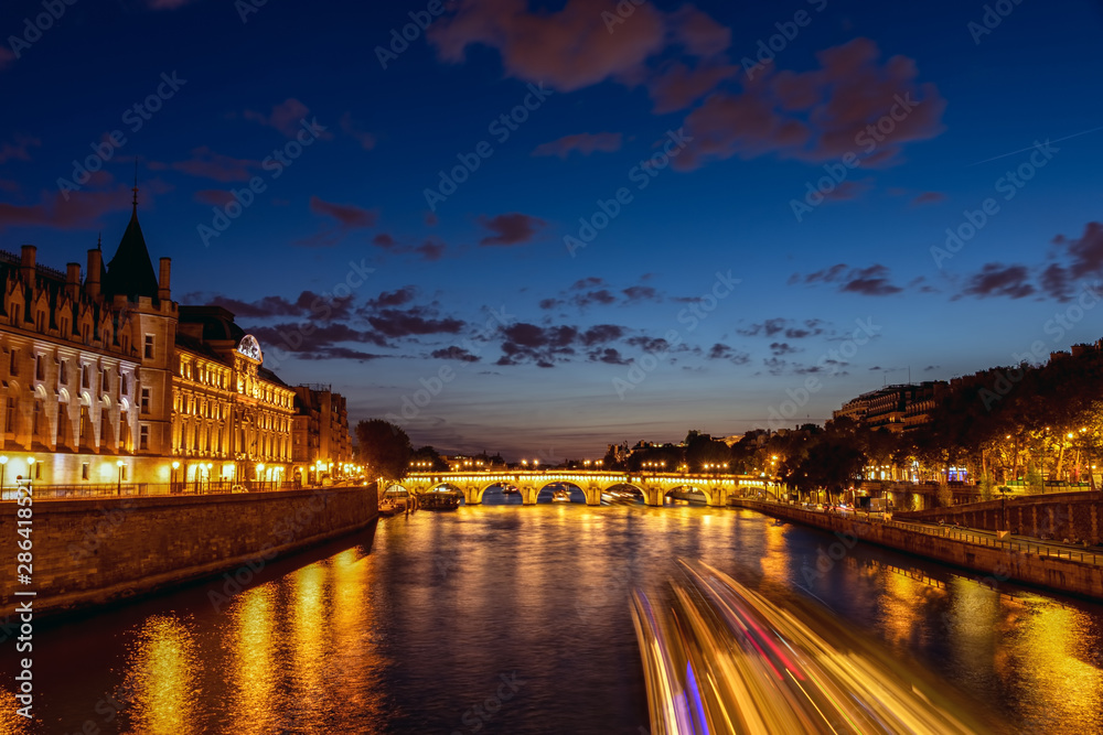 Illuminated Conciergerie and Pont Neuf bridge at night - Paris, France.