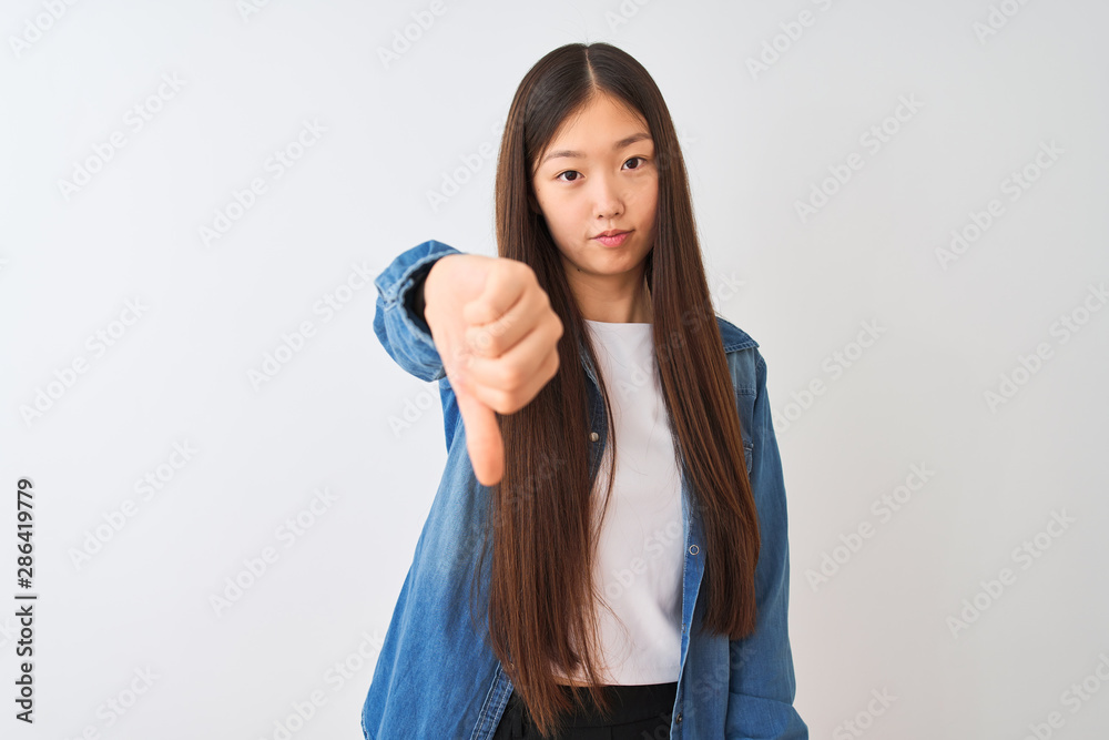 Young chinese woman wearing denim shirt standing over isolated white background looking unhappy and angry showing rejection and negative with thumbs down gesture. Bad expression. Young chinese woman wearing denim shirt standing over isolated white background looking unhappy and angry showing rejection and negative with thumbs down gesture. Bad expression.