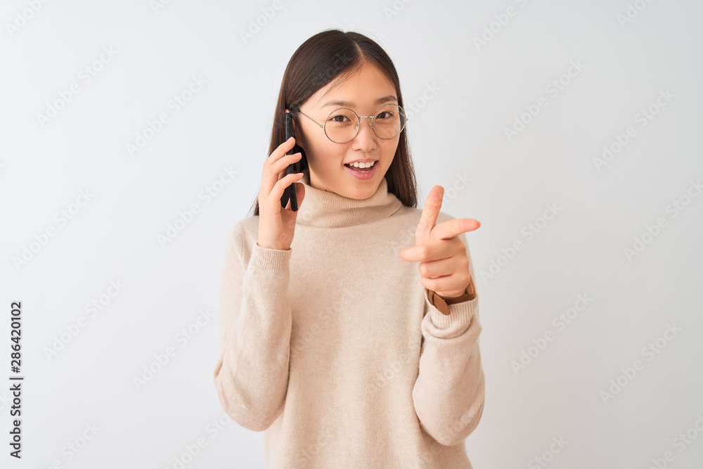Young chinese woman talking on the smartphone over isolated white background pointing fingers to camera with happy and funny face. Good energy and vibes. Young chinese woman talking on the smartphone over isolated white background pointing fingers to camera with happy and funny face. Good energy and vibes.