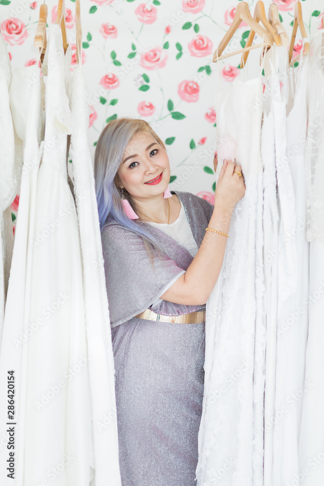 Fototapeta premium Bride is poses among white wedding dresses..