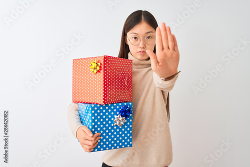 Fotografie Young chinese woman holding birthday gifts over isolated white background doing stop sing with palm of the hand
