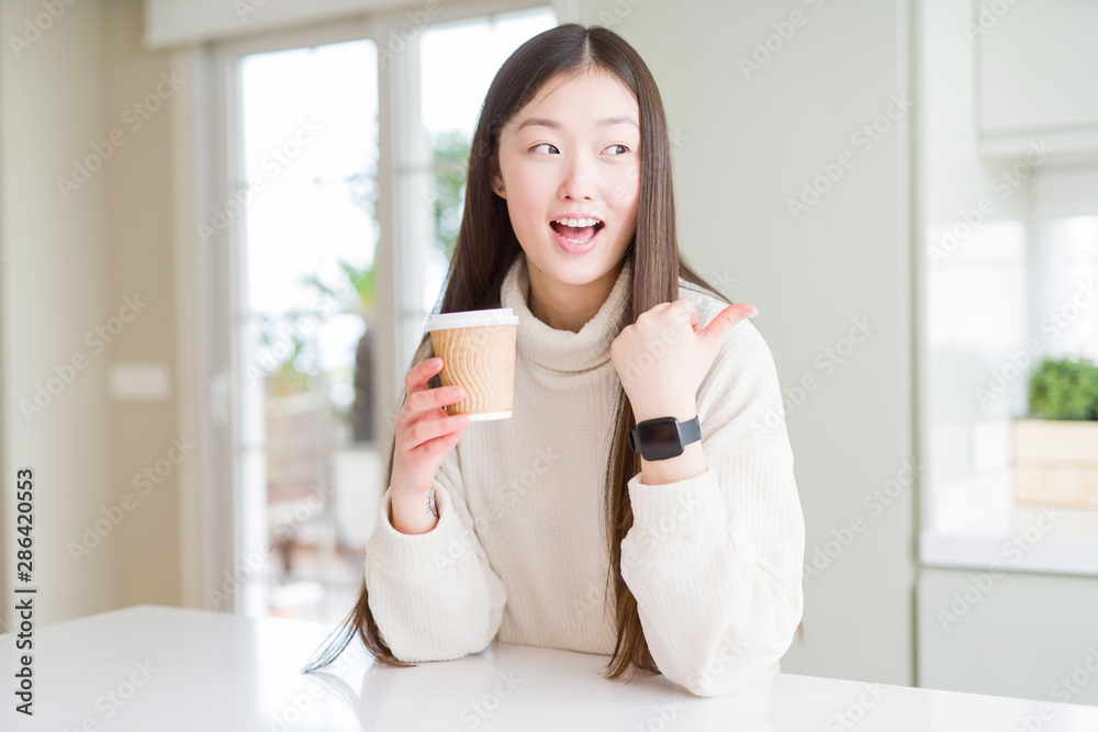 Beautiful Asian woman drinking a coffee in a take away paper cup pointing and showing with thumb up to the side with happy face smiling Beautiful Asian woman drinking a coffee in a take away paper cup pointing and showing with thumb up to the side with happy face smiling