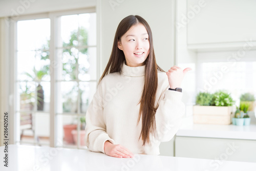 Beautiful Asian woman wearing casual sweater smiling with happy face looking and pointing to the side with thumb up.