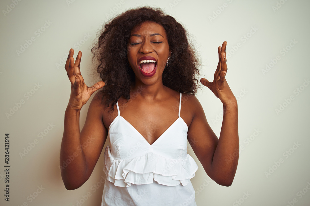 Young african american woman wearing t-shirt standing over isolated white background celebrating mad and crazy for success with arms raised and closed eyes screaming excited. Winner concept Young african american woman wearing t-shirt standing over isolated white background celebrating mad and crazy for success with arms raised and closed eyes screaming excited. Winner concept