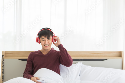 Asian man listen to music by headphone in bedroom..