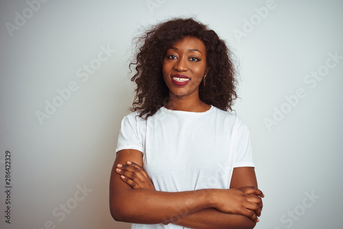 Young african american woman wearing t-shirt standing over isolated white background happy face smiling with crossed arms looking at the camera. Positive person.