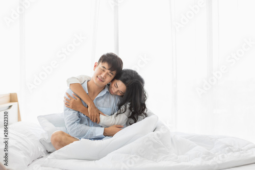 Couplesitting on bed, they hug each other by love..