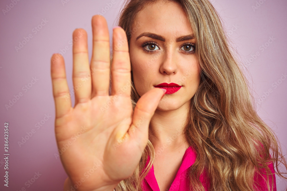 Young beautiful woman wearing elegant shirt standing over pink isolated background with open hand doing stop sign with serious and confident expression, defense gesture