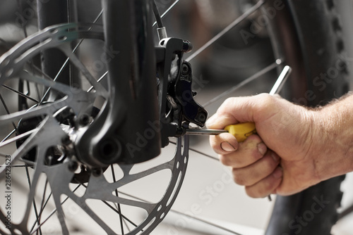 Cropped shot view of a man's hand working in bicycle repair shop, worker repairing modern bike brakes using special tool
