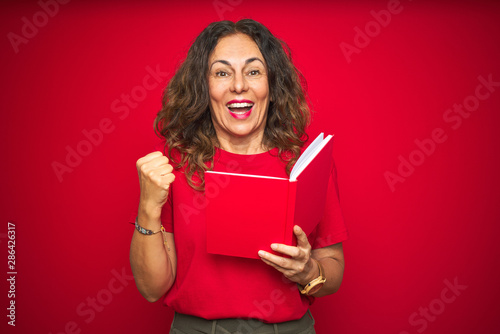 Middle age senior woman reading a book over red isolated background screaming proud and celebrating victory and success very excited, cheering emotion