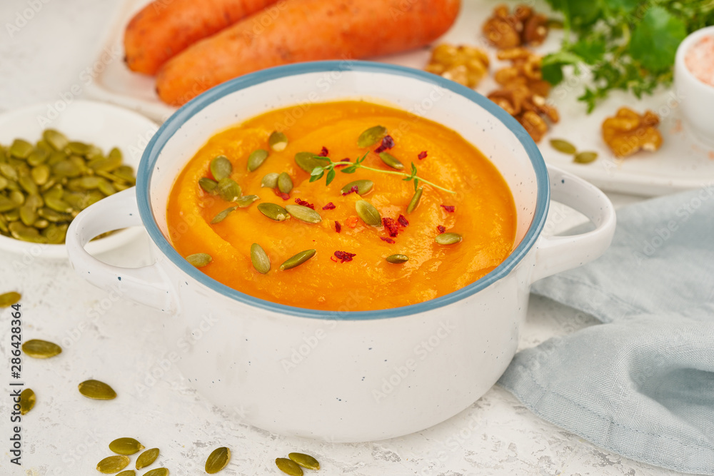 Carrot cream soup with pumpkin seeds and parsley and walnuts, side view on light background closeup Carrot cream soup with pumpkin seeds and parsley and walnuts, side view on light background closeup